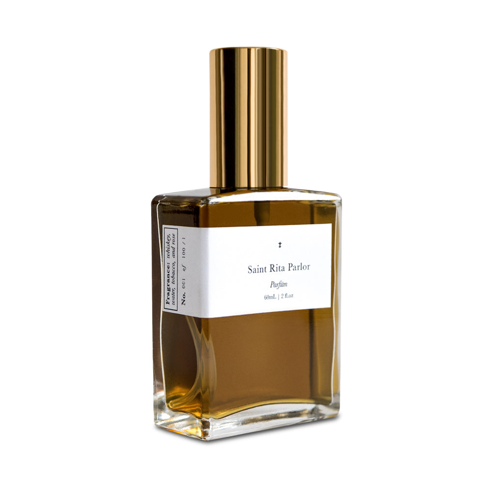 A bottle of Saint Rita Parlor Signature Fragrance Parfum with a golden liquid visible inside, a gold-colored cap, and a white label.