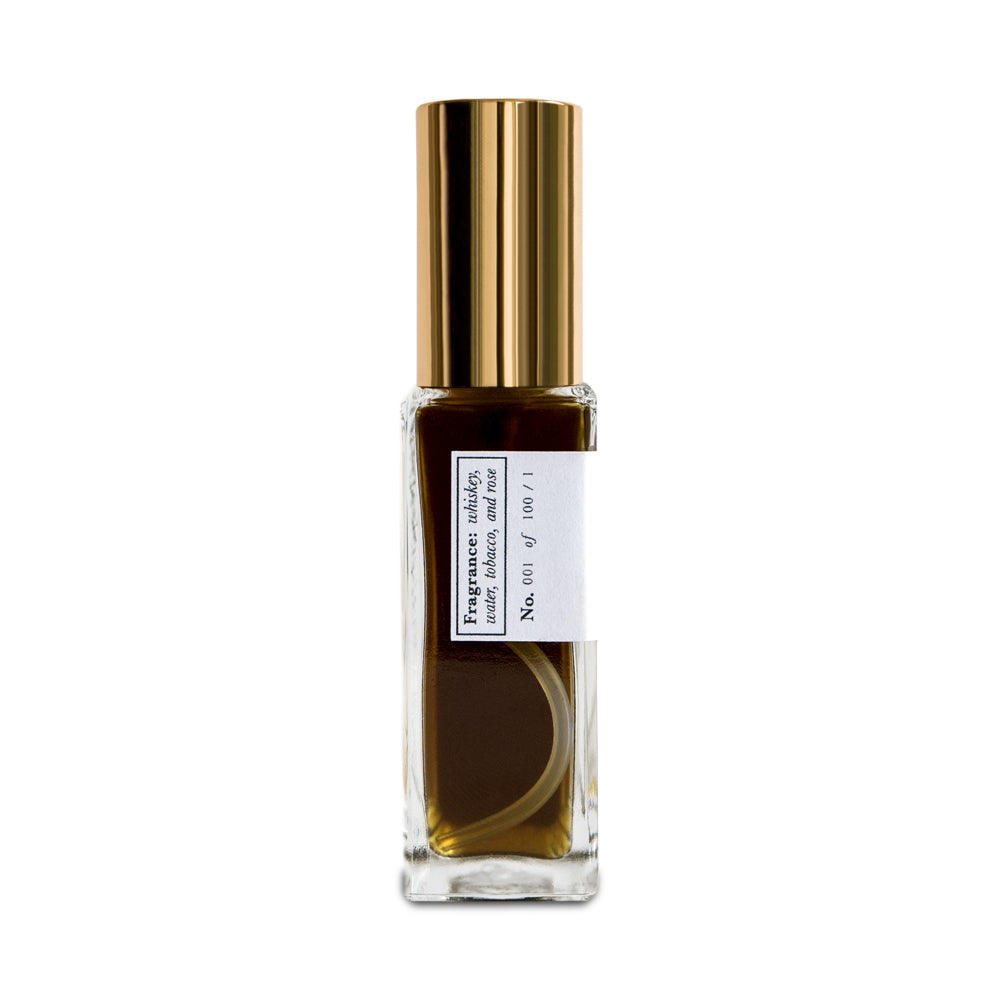 A side view of a bottle of Saint Rita Parlor Signature Fragrance Parfum with a golden liquid visible inside, a gold-colored cap, and a white label.