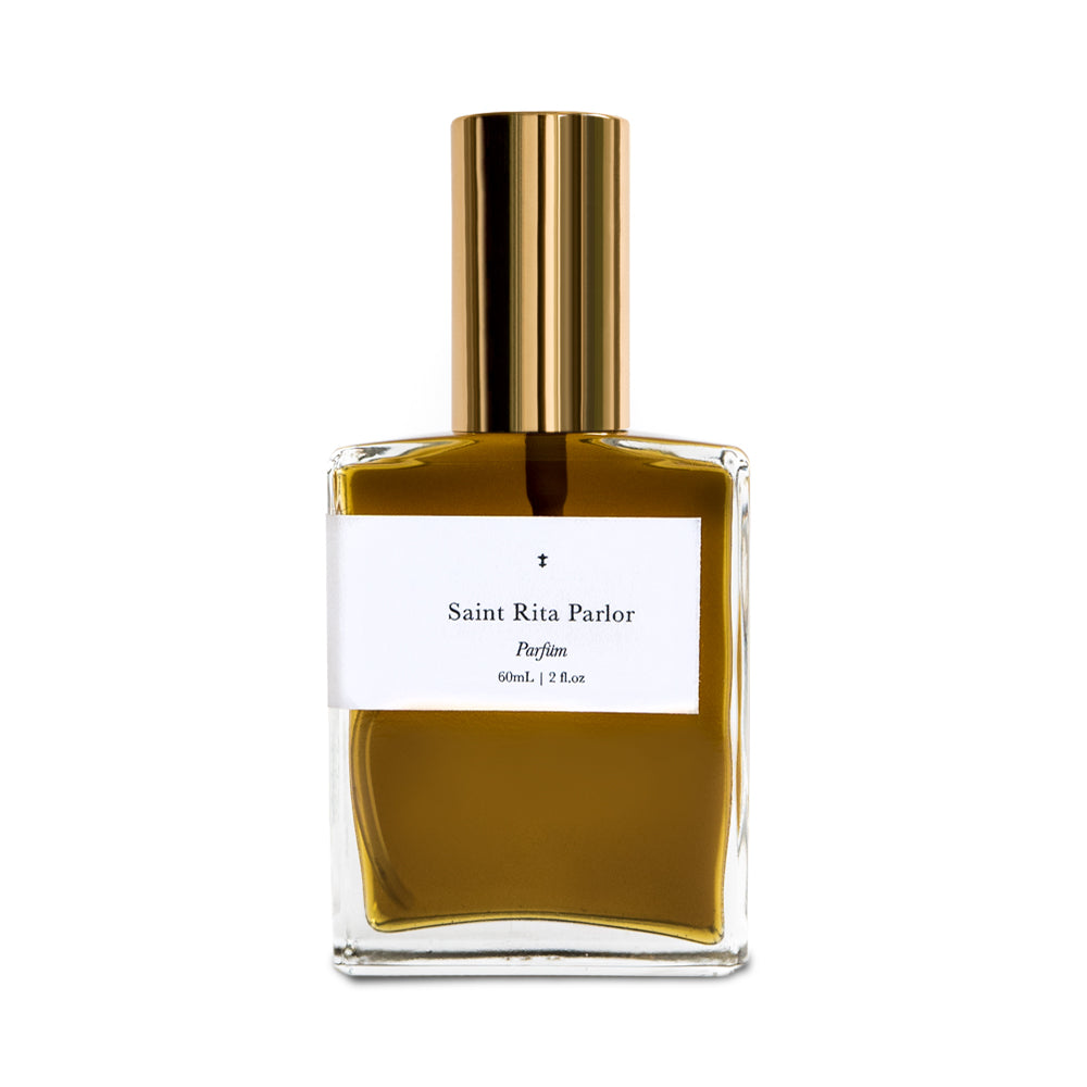 A bottle of Saint Rita Parlor Signature Fragrance Parfum with a golden liquid visible inside, a gold-colored cap, and a white label.