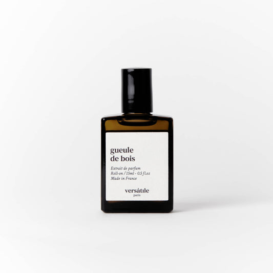 An image of a brown perfume bottle with a black screw on lid on it. The bottle has a square white label on it that says the scent of the perfume 'gueule de bois' along with the amount of perfume in the bottle, that being 15ml and where the perfume was made, that being in France. Beneath this it says versatile Paris.