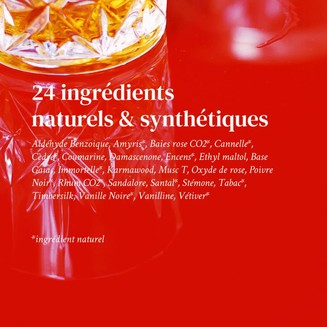 An image of the list of the 24 ingredients that are used to create this perfume, written in French, against the backdrop of a red table with a crystallised glass with brown liquid inside of It.