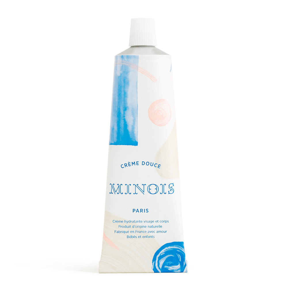 A white squeeze tube with patterns of blue and pink circles, cream and pink lines and blue squares in front of a white background. On the tube, in blue, it says Creme Douce, followed by Minois beneath that and Paris beneath that. Underneath Paris, still in blue in French it lists its child suitability, the natural ingredients and where it was made.