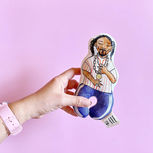 A hand holding a colorful baby rattle designed to resemble a character, with a pink background.
