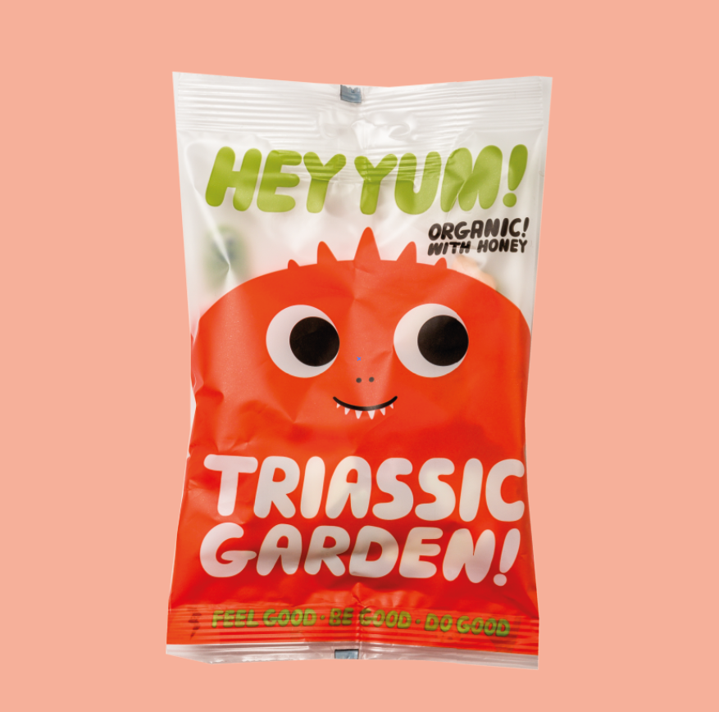 Packaging of HEY YUM! organic fruit marshmallows with a dinosaur shape and fruity flavors. The package is predominantly orange with an illustration of a smiling marshmallow character.