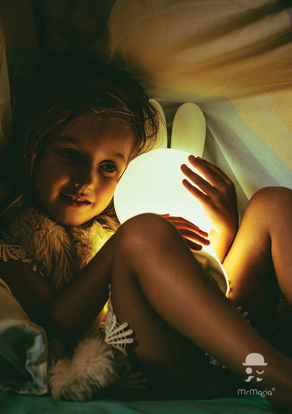 A white Miffy First Light Lamp with a soft glow, shaped like a rabbit held by a young girl under a blanket