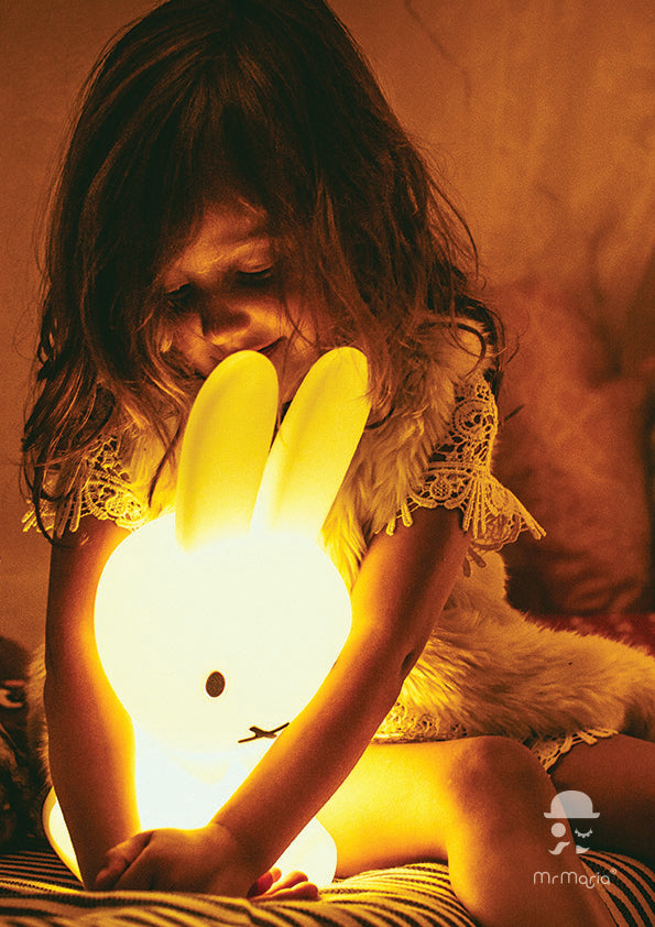 A white Miffy First Light Lamp with a bright glow, shaped like a rabbit with long ears and a simple black-lined face, held by a young girl looking down