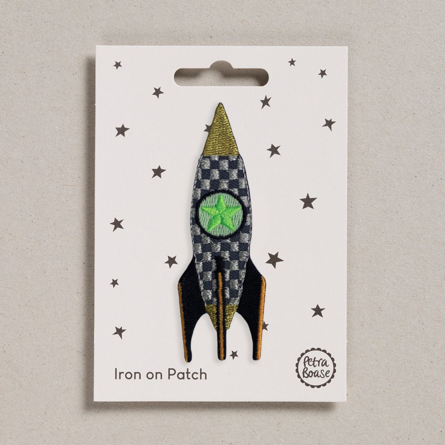an embroidered rocket which has a dark and light grey checkered pattern with black wings and orange lines on them. There is a green star in the middle. The background is white with black stars.