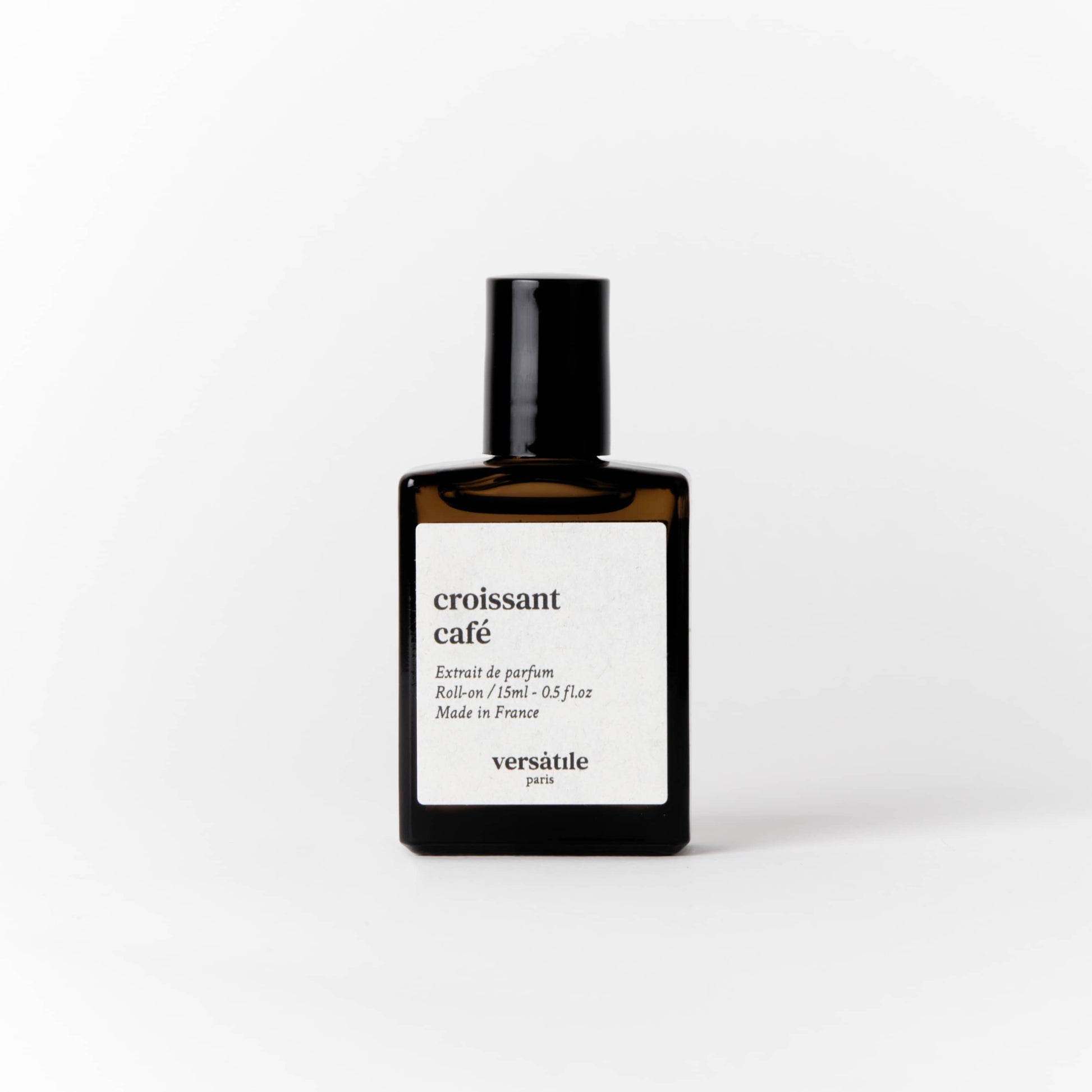 An image of a brown perfume bottle with a black screw on lid on it. The bottle has a square white label on it that says the scent of the perfume 'croissant cafe' along with the amount of perfume in the bottle, that being 15ml and where the perfume was made, that being in France. Beneath this it says versatile Paris.