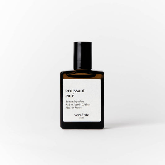 An image of a brown perfume bottle with a black screw on lid on it. The bottle has a square white label on it that says the scent of the perfume 'croissant cafe' along with the amount of perfume in the bottle, that being 15ml and where the perfume was made, that being in France. Beneath this it says versatile Paris.