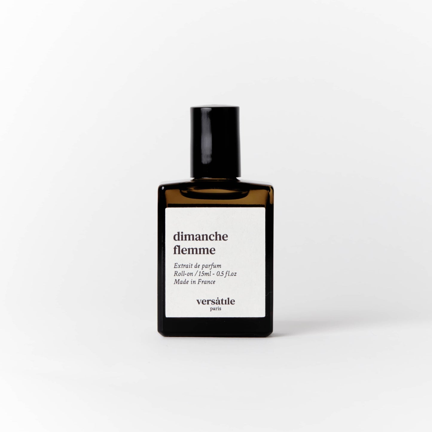 An image of a brown perfume bottle with a black screw on lid on it. The bottle has a square white label on it that says the scent of the perfume 'dimanche flemme' along with the amount of perfume in the bottle, that being 15ml and where the perfume was made, that being in France. Beneath this it says versatile Paris.