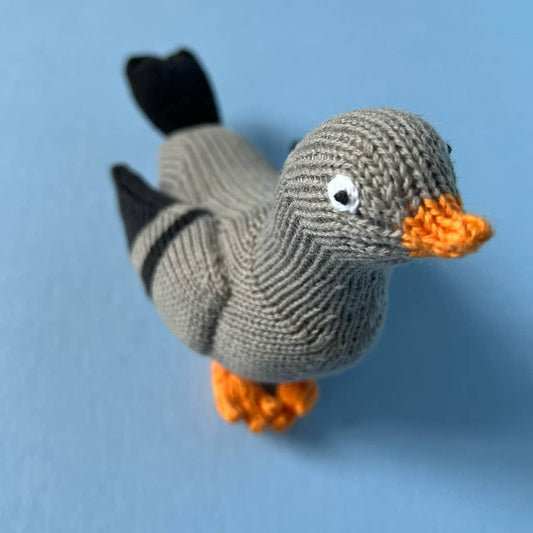 Knitted toy duck with orange beak and feet on a blue background