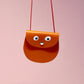 Small brown leather bag with googly eyes on a pink background