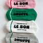 Four pairs of socks in pink, green, white, and gray with text on a white background