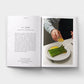 Open book showing a recipe for asparagus with a person garnishing it.