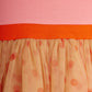Close-up of a pink top with an orange waistband and a peach skirt with red polka dots.