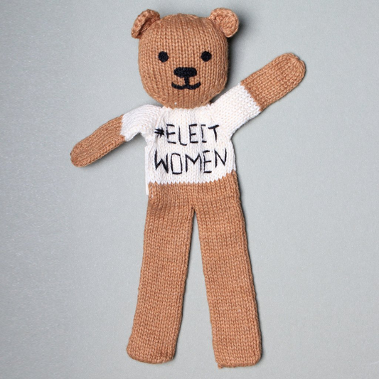 Knitted teddy bear wearing a shirt with '#ELECT WOMEN' text on a gray background