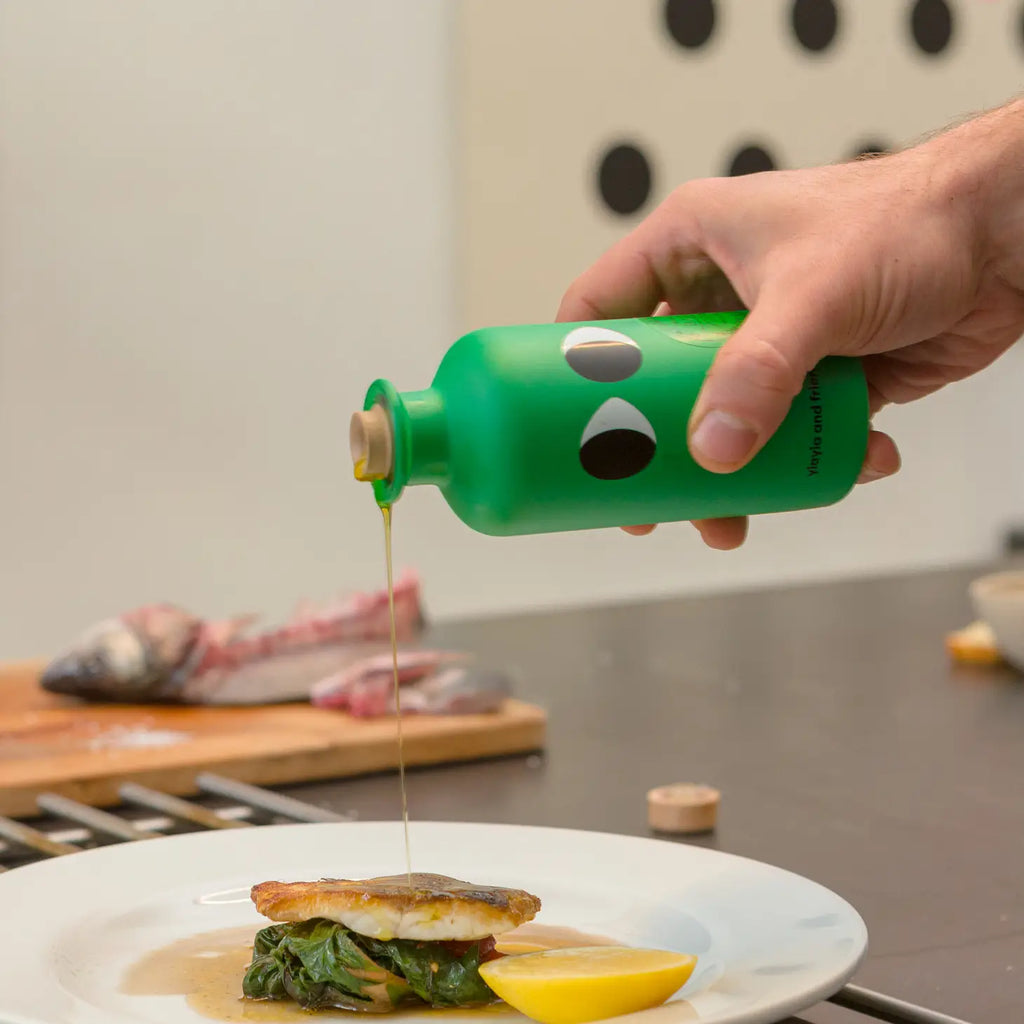 Person pouring syrup from a green bottle with a face design onto a plate of food.