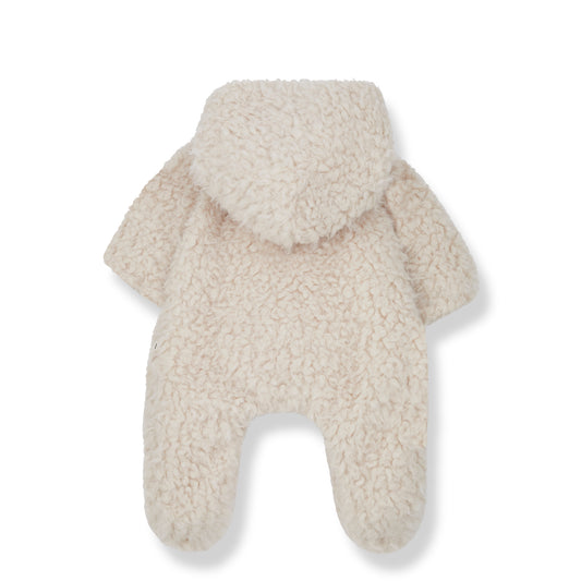 on a white backdrop, a fluffy fleece one piece jumpsuit. with covered feet and open hands, a little bow wrap over front and a hood, all in a creamy tone