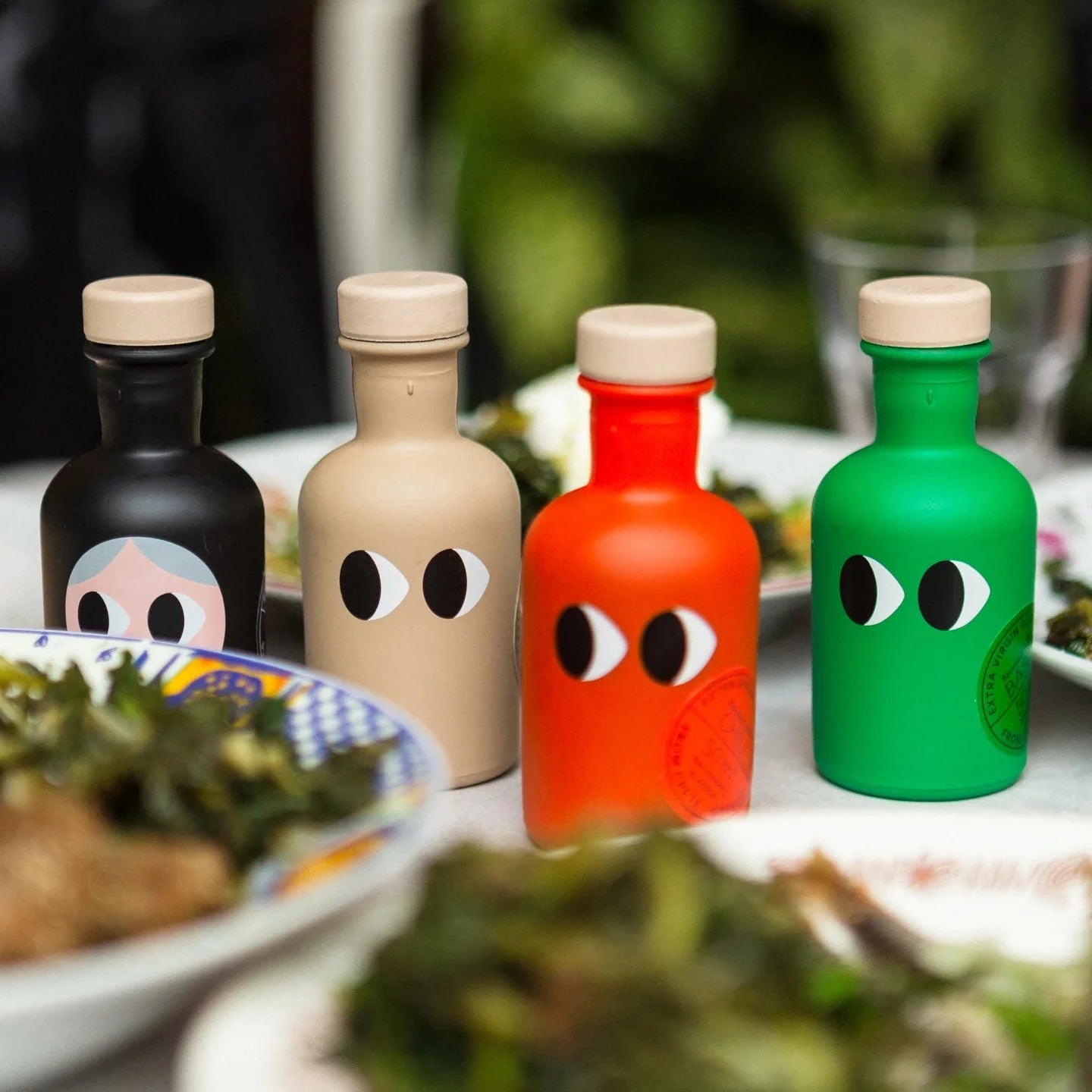 Four colorful bottles with face-like designs on a table with food.