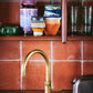 A collection of HKliving 70's ceramics sits on a shelf in a brown tiled kitchen in front of a gold curved tap