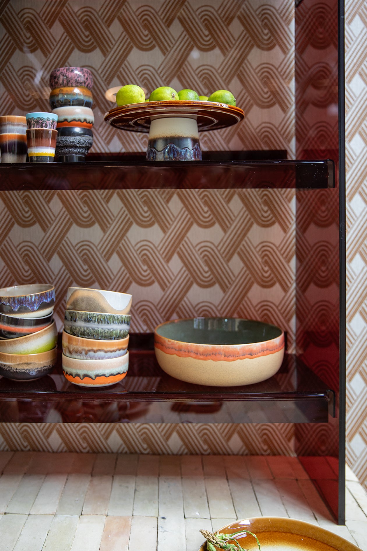 In this images is a variety of Hk living bowls, mugs and a cake stand. On two shiny shelves infornt of a retro brown wall paper 