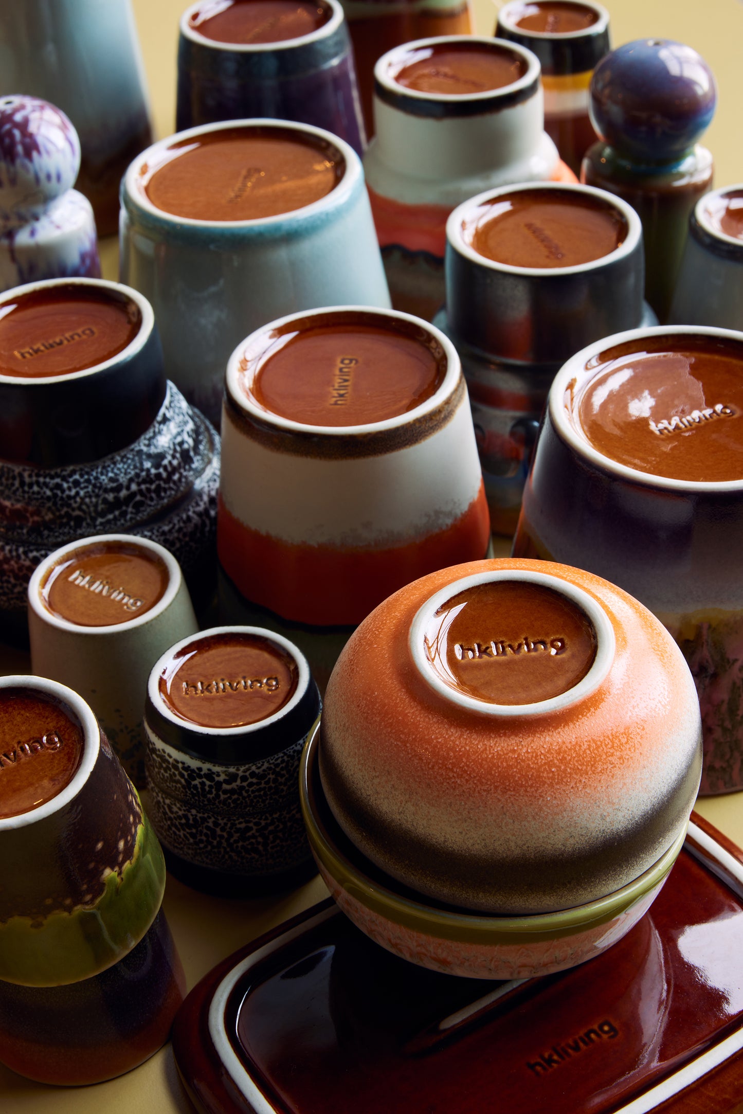 In this image there is a flat lay of a variety of Hk living mugs all turned over showing their embossed logo on the bottoms in a deep brown glase