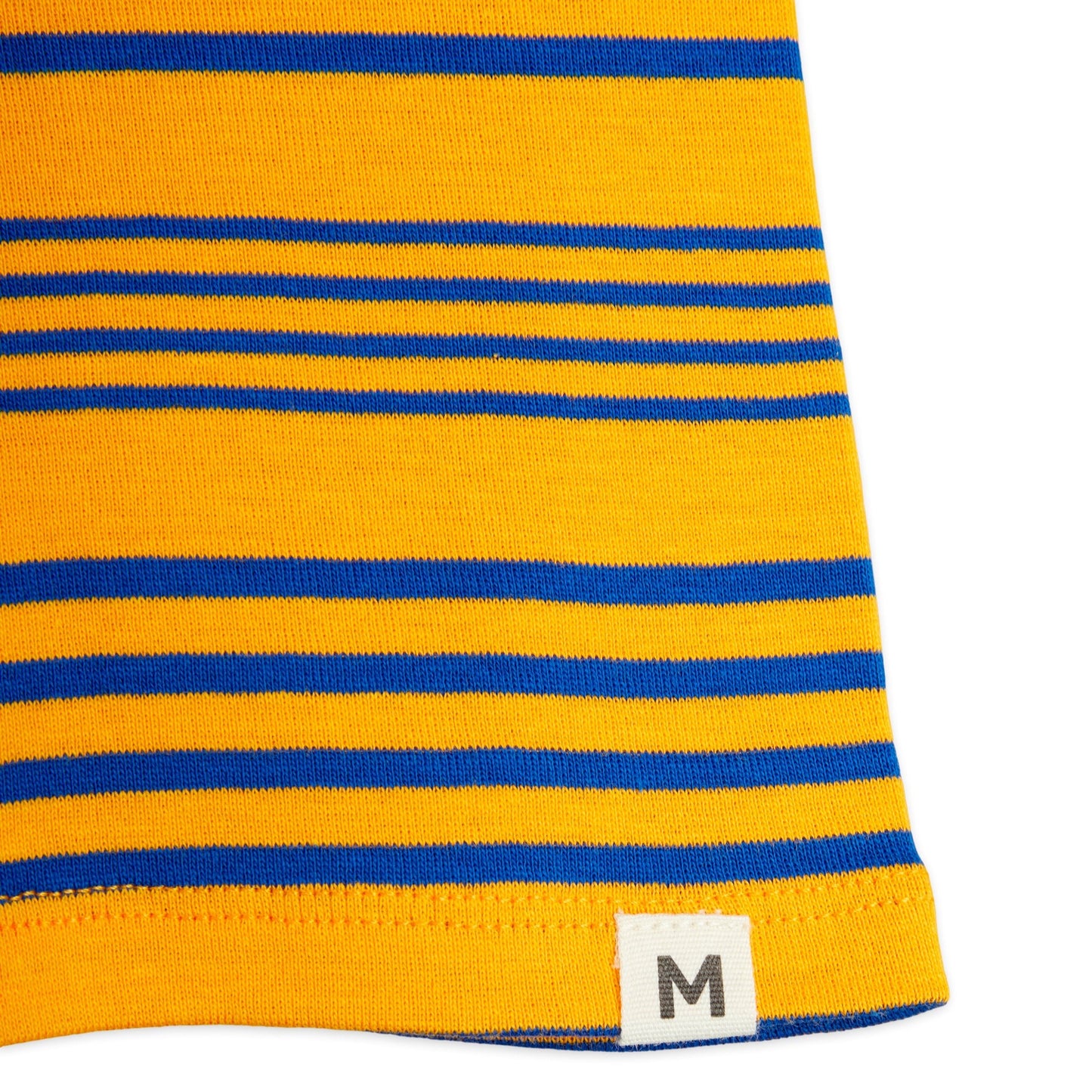 Detailed view of the hem on the Mini Rodini striped bike shorts, featuring a small white fabric tag with an "M" logo and a neat stitched edge.