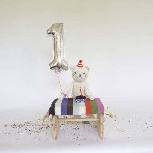 Stuffed teddy bear with a striped blanket and number one balloon on a white background
