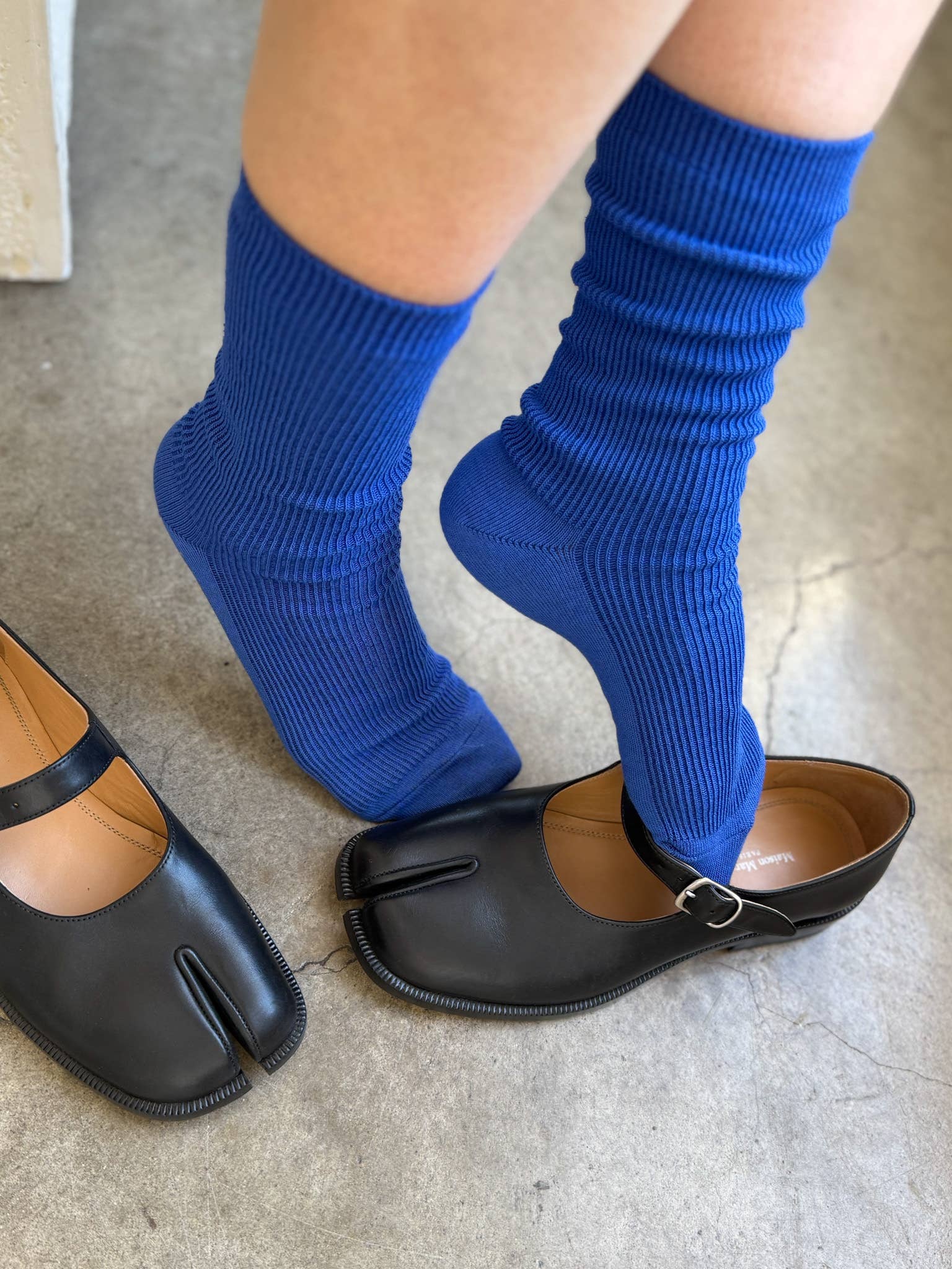Person wearing blue socks and black open-toe shoes on a neutral background