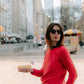 Woman in a red sweater holding a pastry on a city street