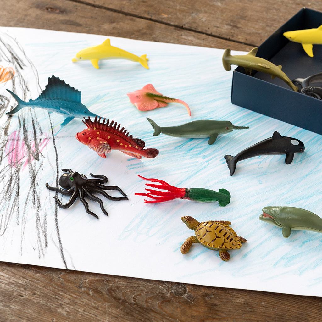 Assorted toy sea creatures on a paper with a wooden surface background