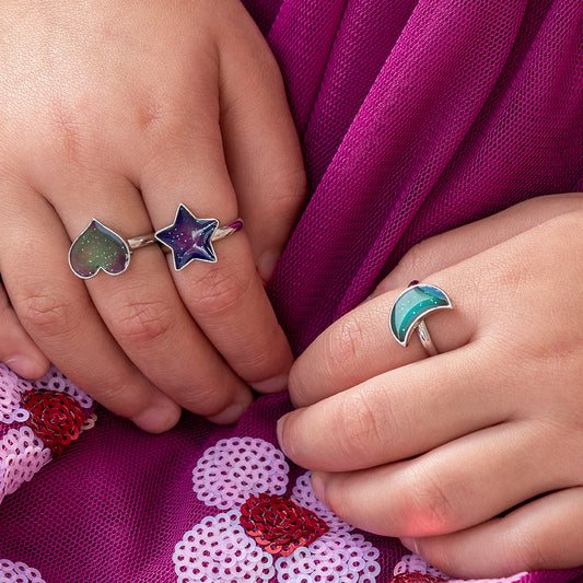 Close-up of two hands wearing colorful rings on a purple fabric background