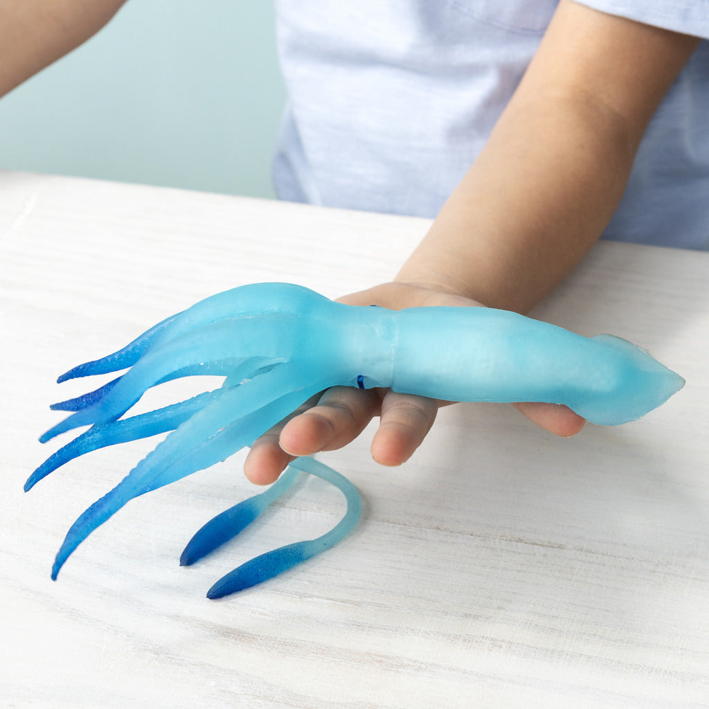 Person holding a blue squid-shaped toy on a white surface