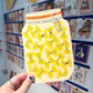 Hand holding a yellow milk carton with butterfly design against a wall with children's artwork.