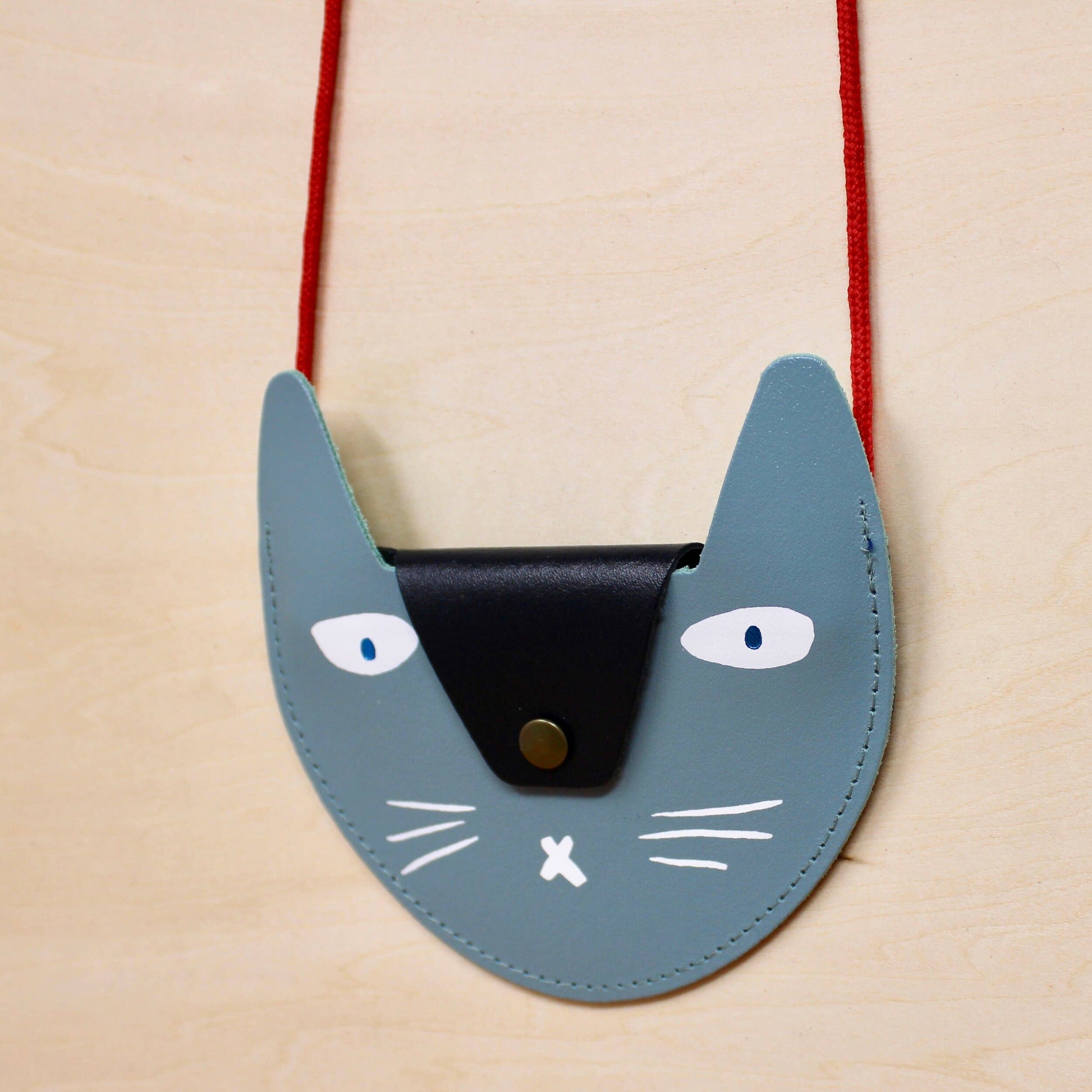 Cat-shaped purse with a red strap on a beige background