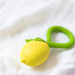 Yellow teething ball with green handles on a white fabric background