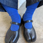 Black tabi shoes worn with blue socks on a neutral background