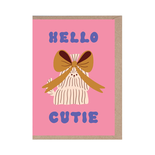 A greeting card with a pink background featuring a playful, bow-topped fluffy creature with the text 'HELLO CUTIE' in bold, blue letters.