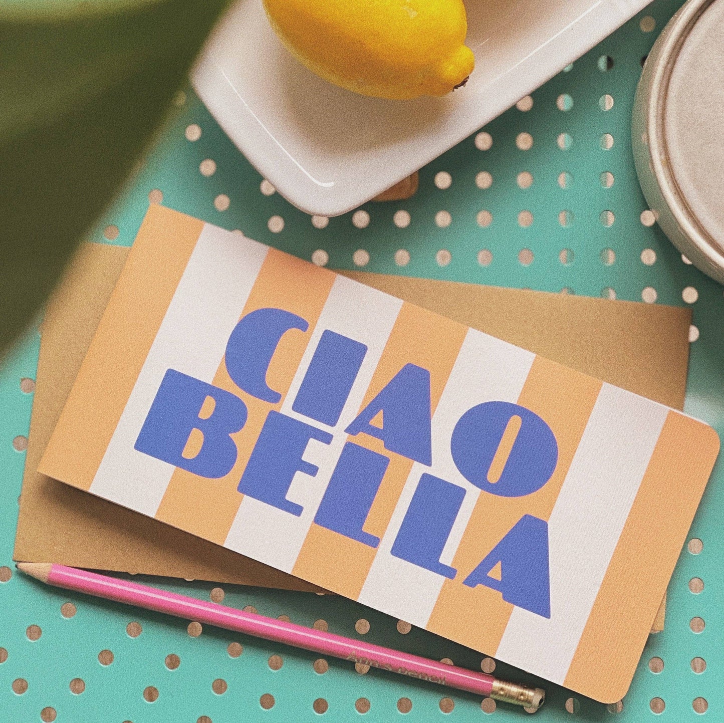 A greeting card with an orange and white striped background. On top of that is the words Ciao Bella in blue writing. 