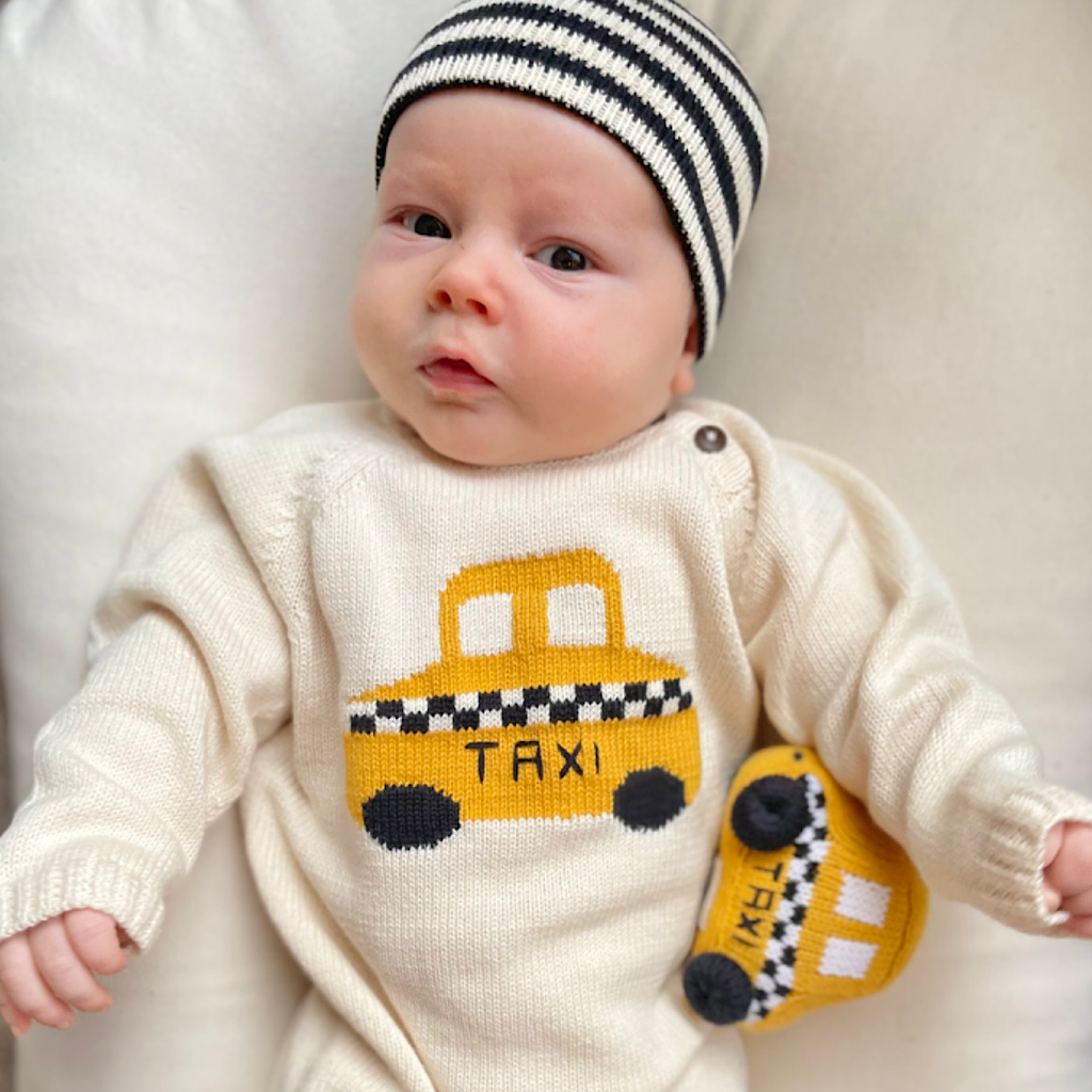 Baby wearing a knitted sweater with a taxi design and a striped hat.