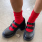 Black shoes with red buckles worn with red socks on a concrete floor.
