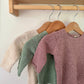 Three knitted sweaters hanging on a rack against a white wall.