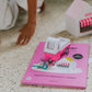 Toy ice cream truck on a pink book with a child's hand reaching towards it.