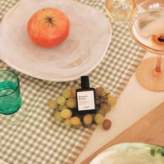 Table setting with fruits, glasses, and a bottle of perfume on a checkered tablecloth.