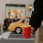 Person holding a red cup with a yellow lid and straw in an urban setting