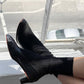 Black ankle boots with orange accents worn by a person sitting on a bench.