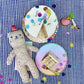 Birthday cake with candles, slice of cake on a plate, and a teddy bear on a checkered tablecloth.