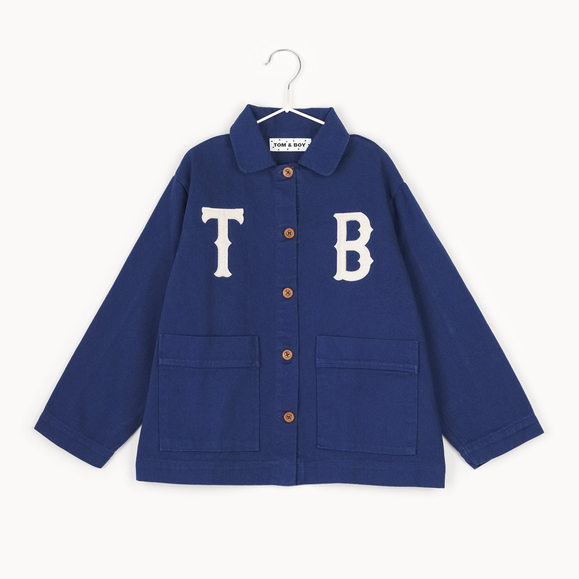 Navy kids chore jacket with oversized white appliqué letters, wooden buttons, and front patch pockets, crafted from organic cotton in Portugal.