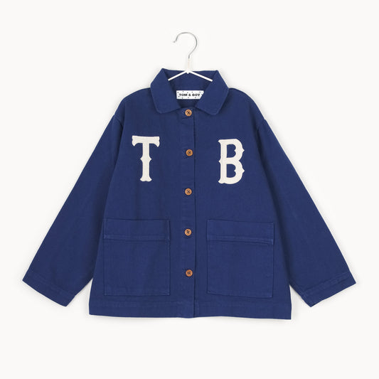 Navy kids chore jacket with oversized white appliqué letters, wooden buttons, and front patch pockets, crafted from organic cotton in Portugal.