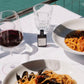 Table with pasta, red wine, and a glass of water by a waterfront.